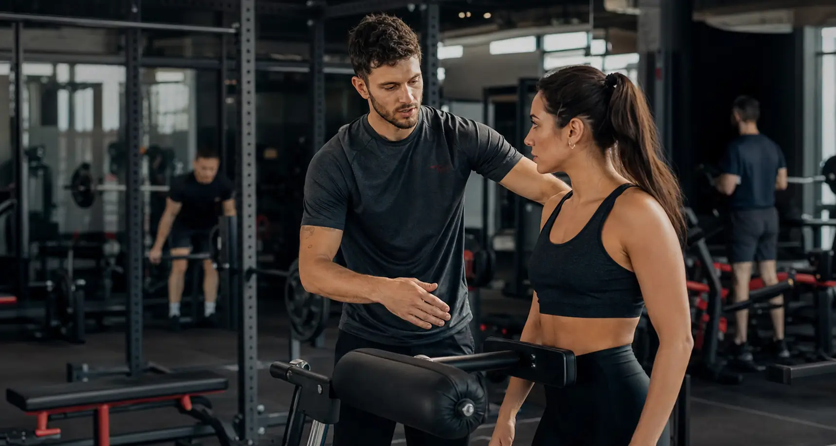 Personal trainer che applica il sistema in palestra con una cliente davanti a un macchinario